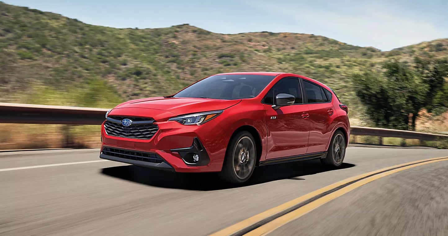 A red Subaru Impreza driving down the road by the plains.