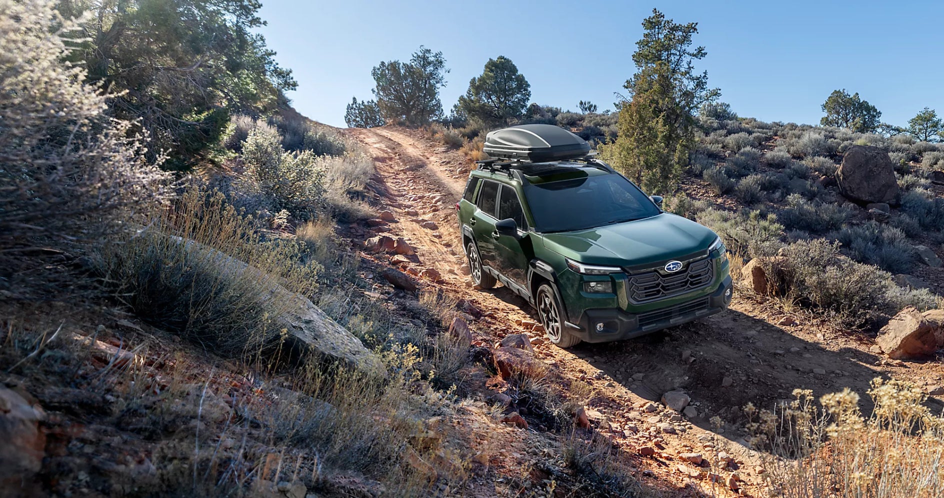 A green Subaru Outback driving down a rocky hill.