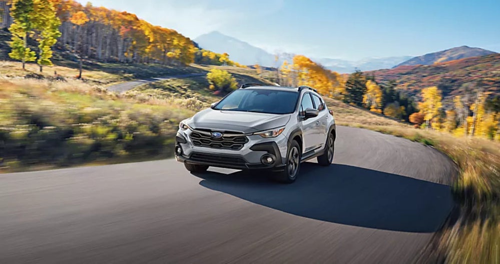A silver Subaru Crosstrek driving down a road.