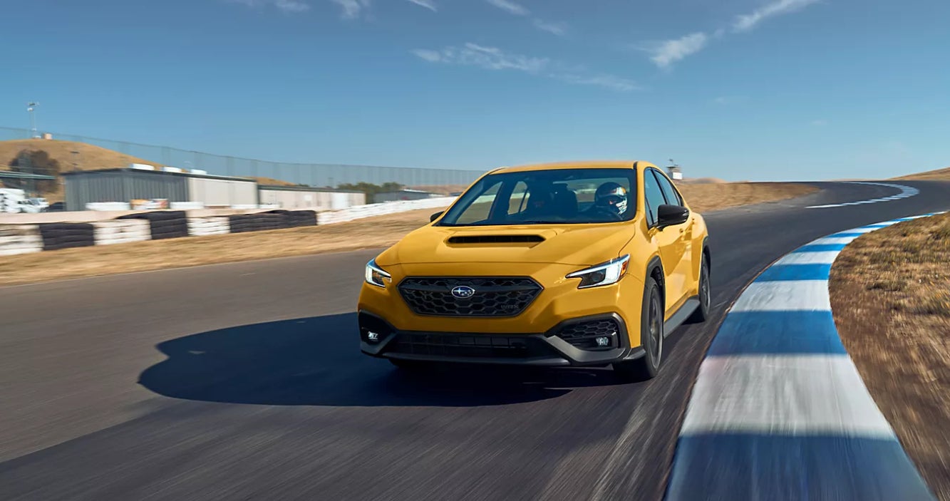 A yellow Subaru WRX driving around a race track.
