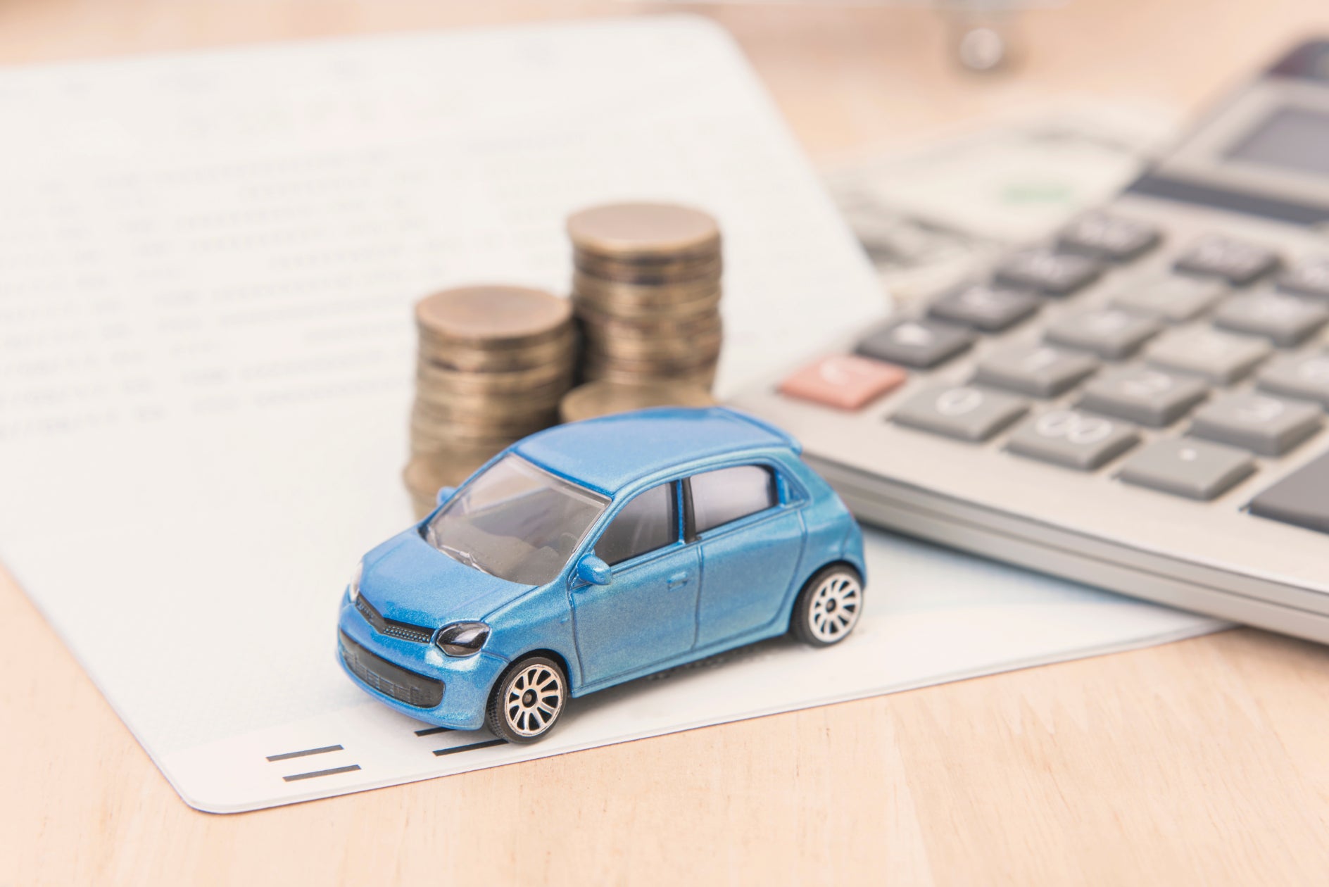 A blue toy car on a desk next to a stack of coins and a calculator.