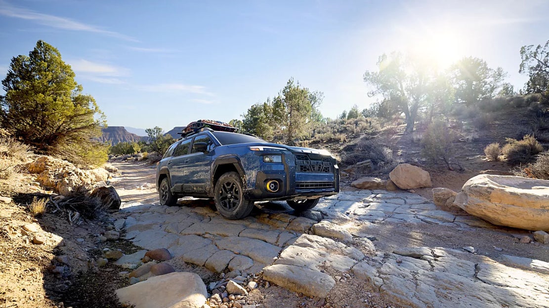 A blue Subaru Outback driving over rocks in a desert.