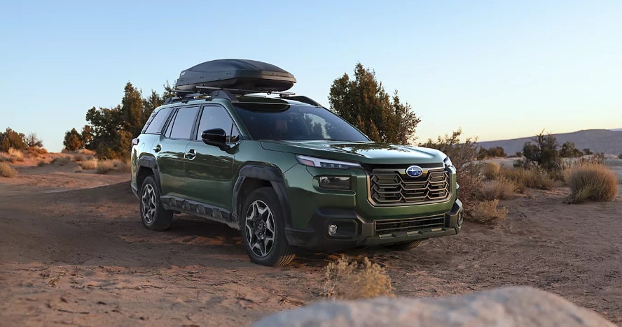 A green Subaru Outback parked in a desert brush.