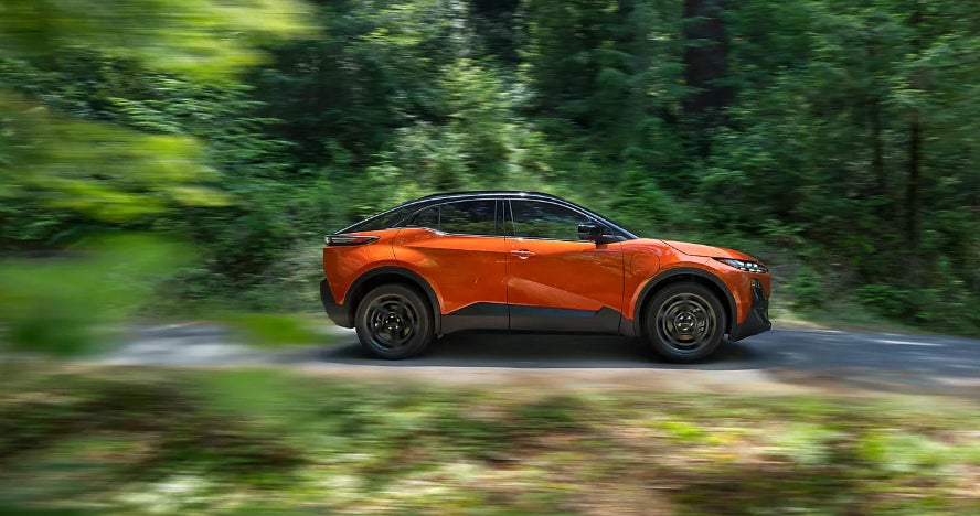 An orange Subaru Uncharted in profile driving down the road through a forest.