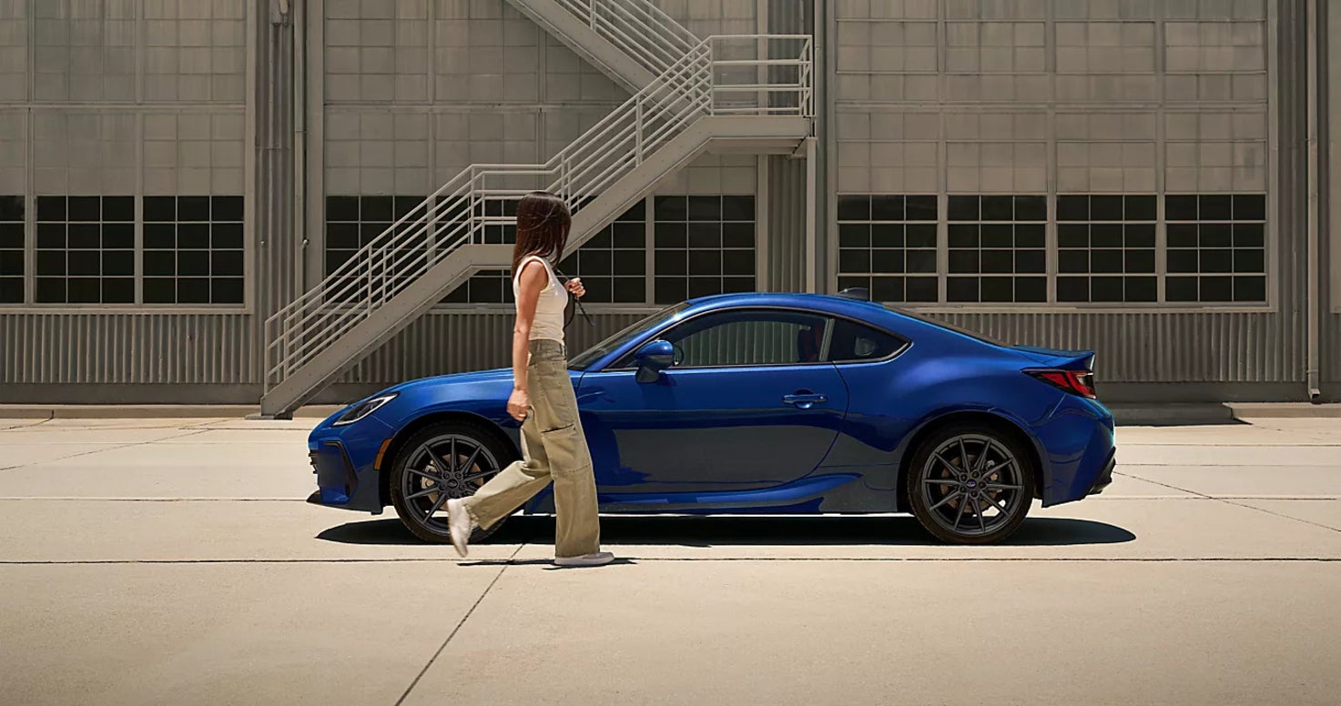 A blue Subaru BRZ in profile with a woman approaching the driver's seat.