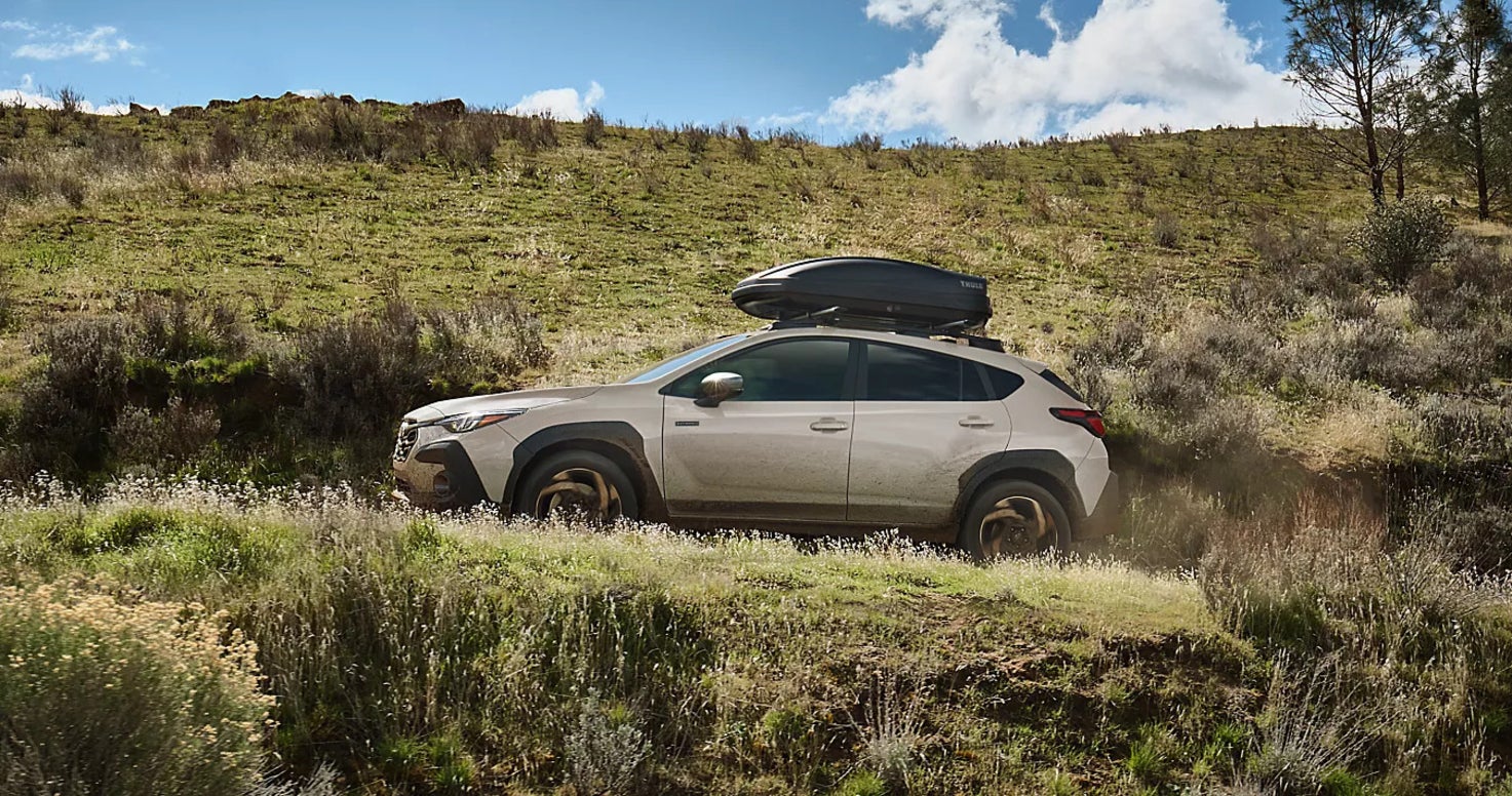 An off-white Subaru Crosstrek driving up a hill in a grassy area.
