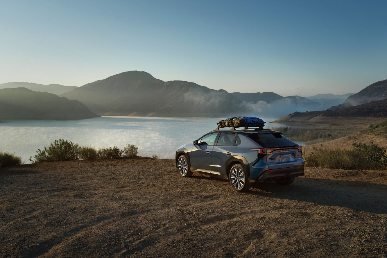 A blue Subaru Solterra parked off-road overlooking a lake.