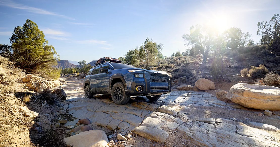 A blue Subaru Outback driving over rocky terrain.