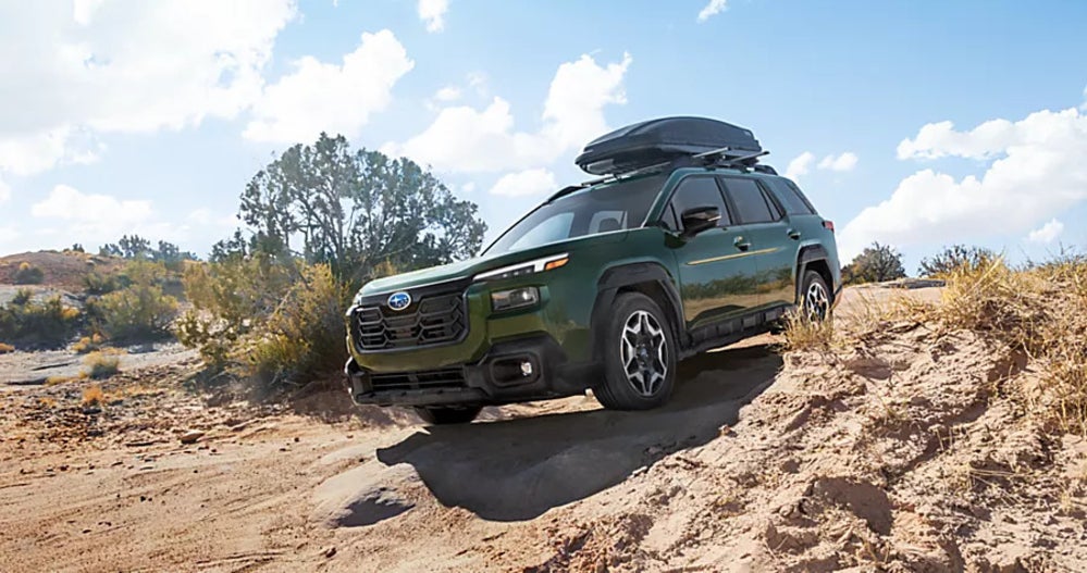 A green Subaru Outback driving off-road over dirt.